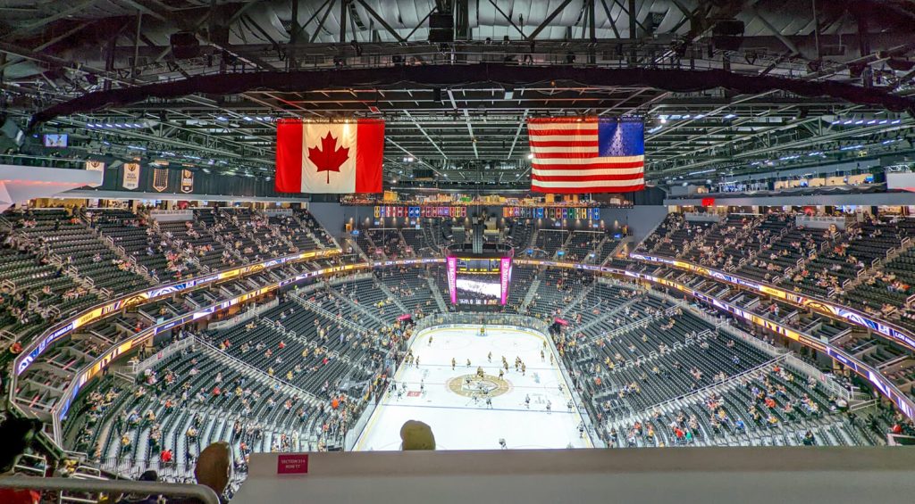 view of T-Mobile arena from the end zone in the upper deck prior to an NHL hockey game. Canada and USA flags visible in rafters, with a scattering of fans in seats prior to gametime.
