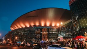 Nighttime view of Bridgestone Arena in Nashville with the entrance lit up in warm lights and crowds gathering outside before an event.