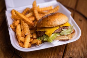 Close-up of a takeout container holding a cheeseburger with lettuce and crinkle-cut fries, placed on a wooden table.