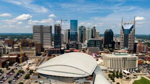 Aerial view of downtown Nashville, Tennessee on a sunny day, with high-rise buildings and construction cranes surrounding Bridgestone Arena.
