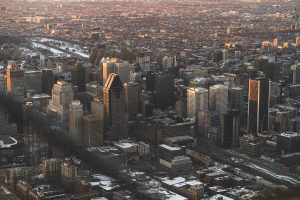 Aerial view of downtown Montreal during the day with sunlight casting warm tones on the tops of high-rise buildings and snow visible on rooftops and streets.