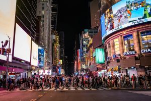 Large crowd of people crossing the street at night in Times Square, New York City, surrounded by bright digital billboards and neon signs