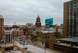 View of downtown Detroit featuring the historic Wayne County Building with green statues on the roof, surrounded by parking lots and modern high-rise buildings under an overcast sky.