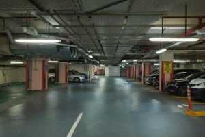 Underground parking garage with multiple parked cars, overhead ventilation, and fluorescent lighting