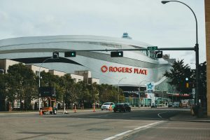 Street view of Rogers Place arena in Edmonton, Alberta, with modern architecture and clear signage under a partly cloudy sky.
