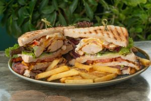Grilled chicken club sandwich with lettuce, tomato, and melted cheese, served with golden French fries on a plate.