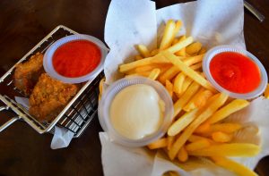 A basket of golden French fries with mayonnaise and chili sauce, next to a metal basket holding crispy fried chicken wings and a side of red dipping sauce.