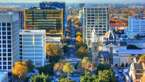 Aerial view of downtown San Jose, California, showing tree-lined streets, tall office buildings, and the historic Cathedral Basilica of St. Joseph with its distinctive domes and towers.