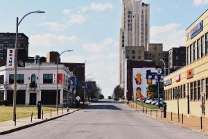 Urban street view in St. Louis showing buildings, murals, and Saint Louis University signs on a sunny day with a mostly clear sky.
