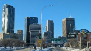 Winter view of downtown Winnipeg, Manitoba, with snow-covered streets, traffic lights, and prominent buildings including the TD and BMO towers.
