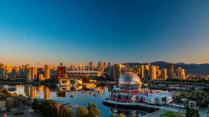 A panoramic view of downtown Vancouver at sunset, featuring BC Place Stadium with its white spiked roof, the reflective waters of False Creek, and the illuminated geodesic dome of Science World in the foreground.