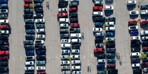 Aerial view of a crowded outdoor parking lot with rows of cars parked closely together, with some people walking between vehicles.