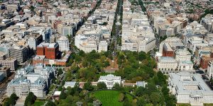 Aerial view of downtown Washington, D.C., featuring the White House in the foreground surrounded by greenery, with city blocks and government buildings extending into the distance.